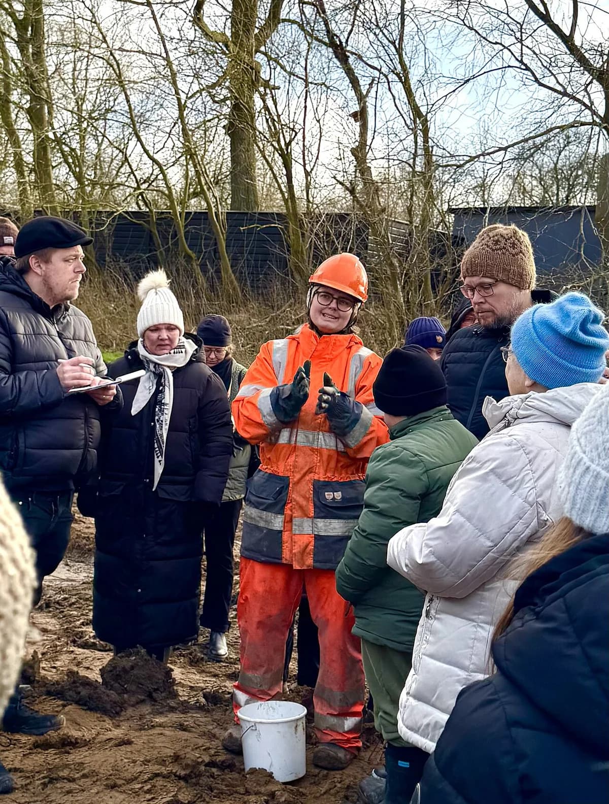 Group at open archaeological excavation site with archaeologist in bright orange gear