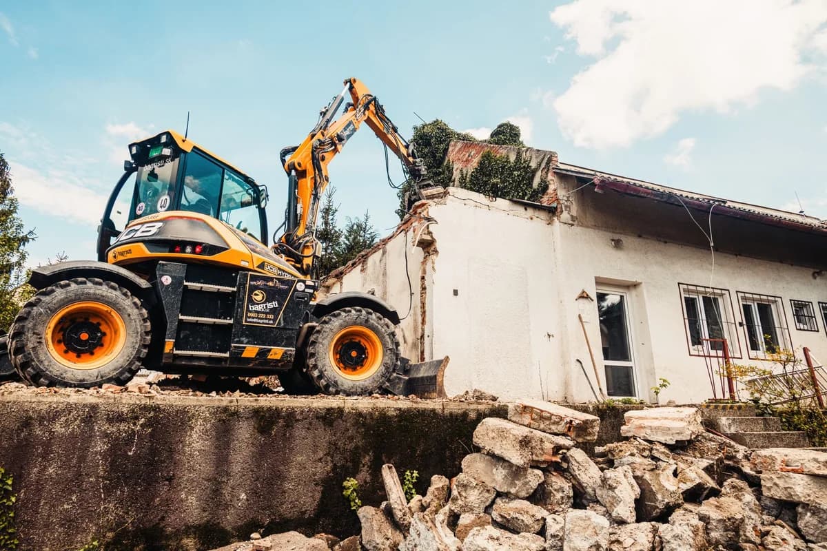 Excavator demolishing an old house with rubble scattered around