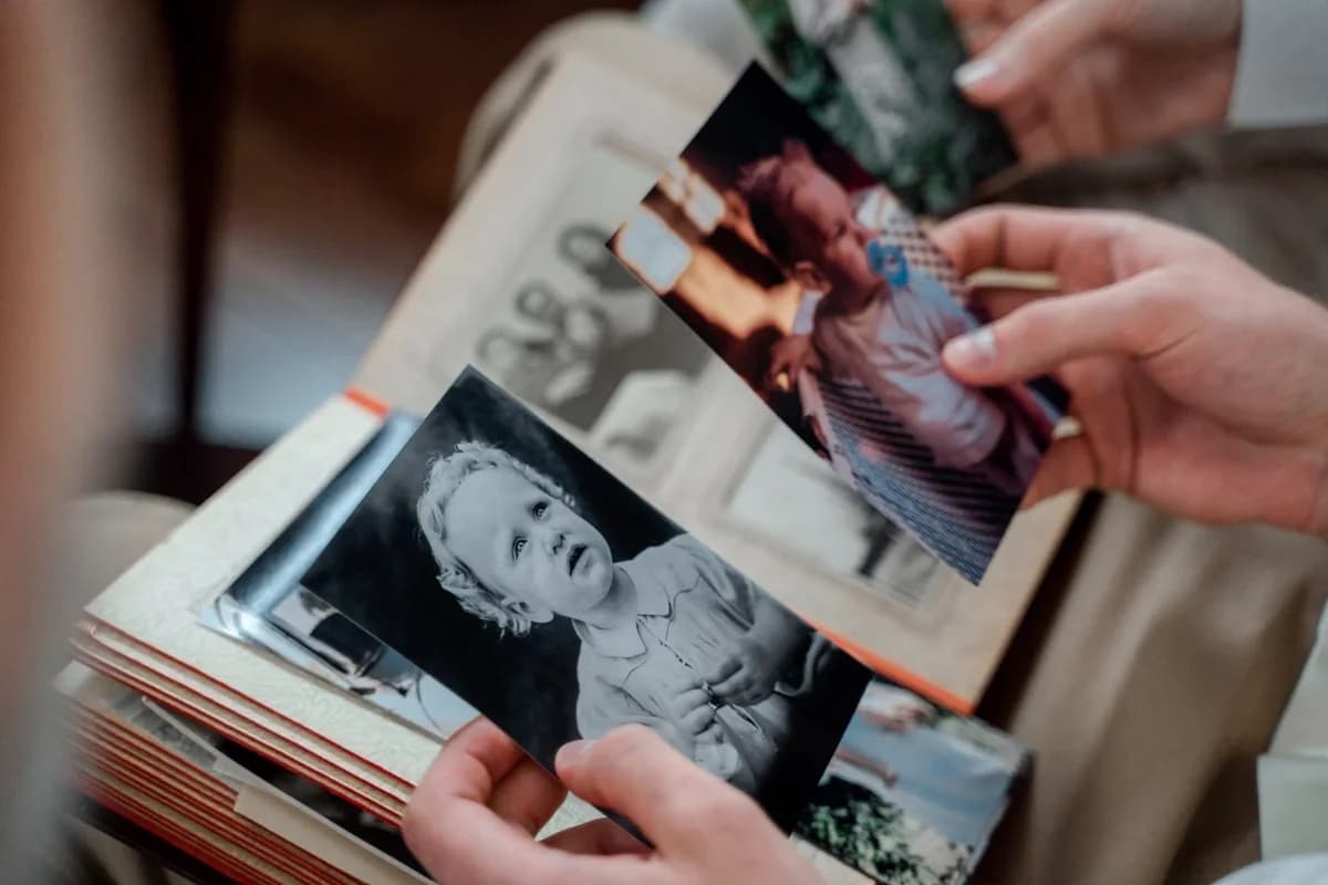 Hands holding old family photos over a photo album.