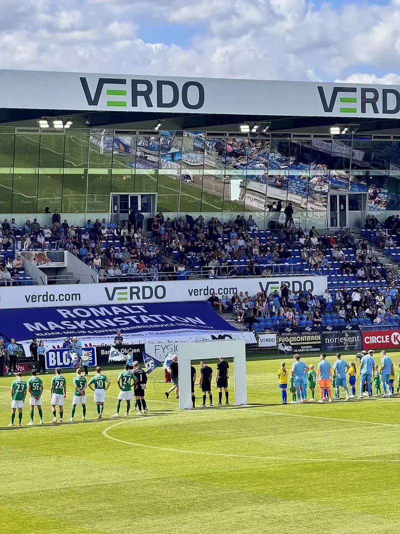 Two soccer teams lined up on the field before a match with VERDO advertisements visible