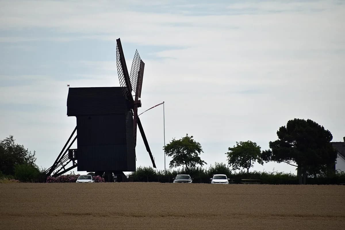 wooden windmill in rural field with cars and trees